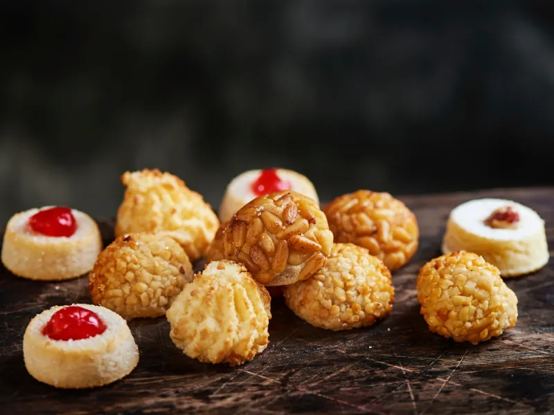Panellets de piñones, almendra, coco y cereza sobre una tabla de madera